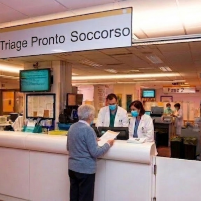 Errore di Triage il peso legale del codice colore errato Personale medico con mascherina al bancone triage di un pronto soccorso mentre parla con un paziente; rappresentazione di errore medico nel codice colore o ritardo nelle cure.